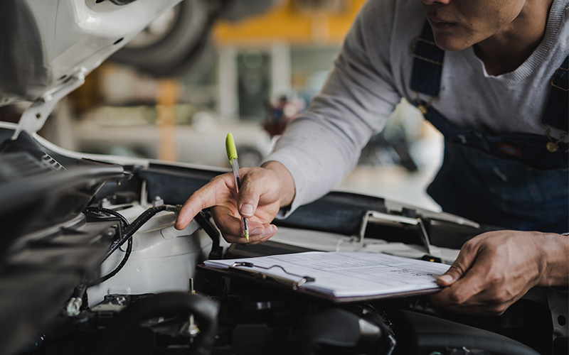 GMC certified mechanic following a checklist to inspect engine of an SUV with pen in-hand
