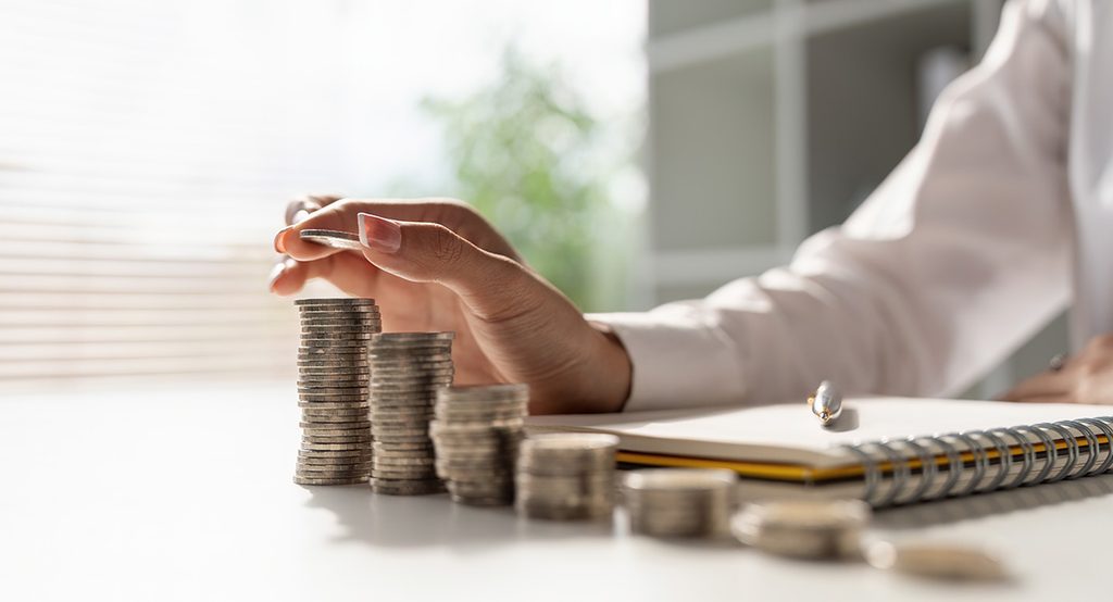 A man in a white shirt is stacking quarters which sit at the top of his notebook and pen as he plans toward GMC New Car Financing.