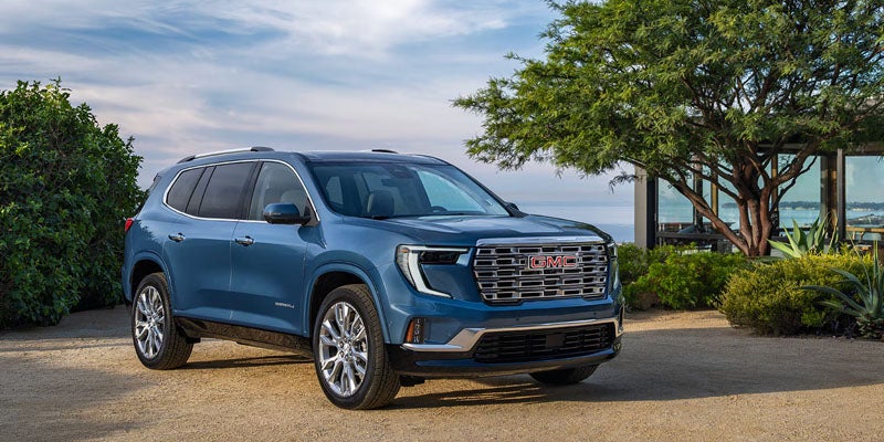 Blue 2026 GMC Acadia parked on a scenic road.